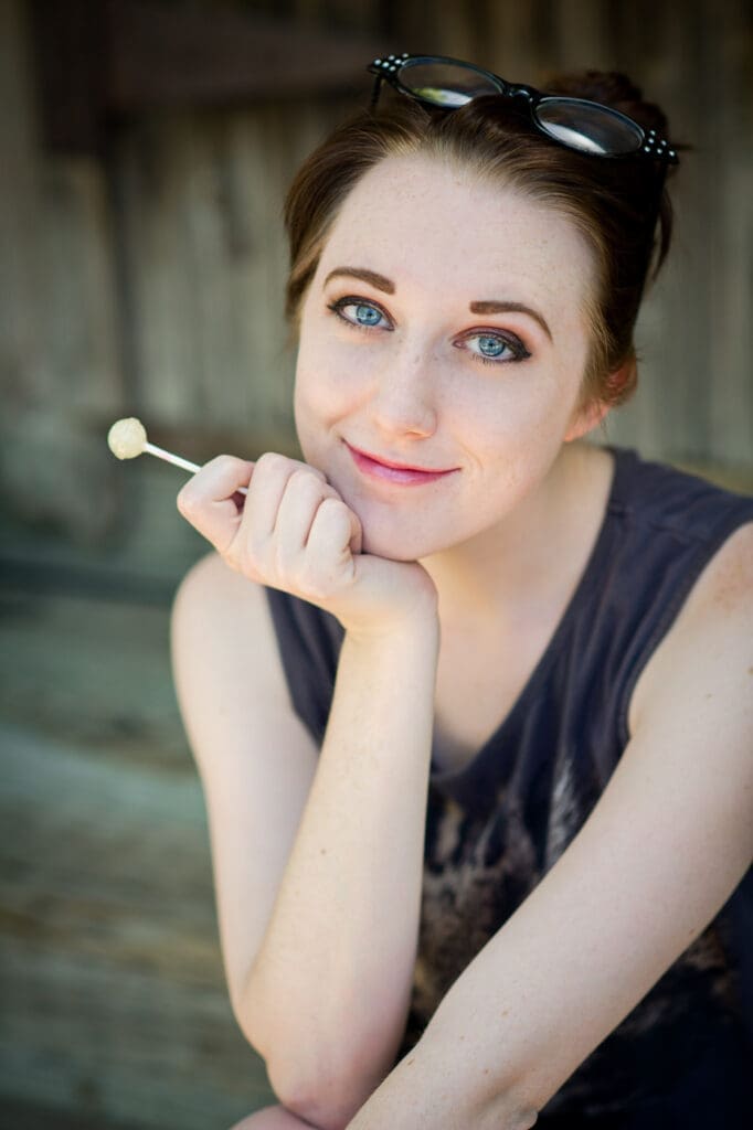 acting headshot pose of a young woman with hands visible holding a lollipop
