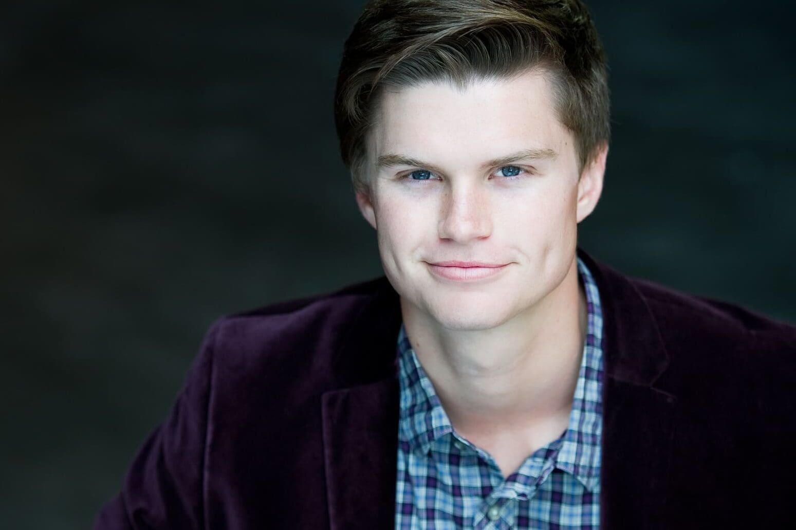 male actor headshot of young man smirking wearing purple velvet jacket