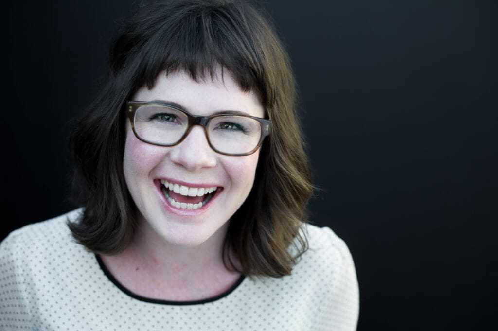 actor headshot of actress with brown hair and glasses laughing